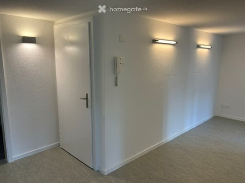 Empty room with white walls, carpeted floor, and a single door. No furniture or equipment is present.