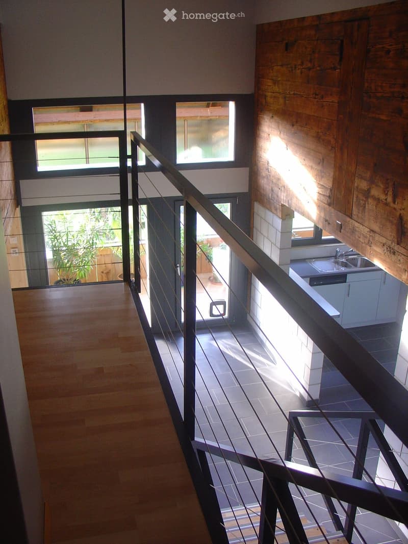 Modern interior hallway with wooden walls, glass railings, and a view of a kitchen area below.