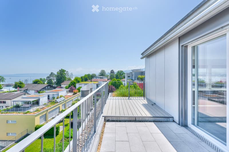 Modern balcony with wooden decking, metal railing, and a view of a waterfront and surrounding buildings.