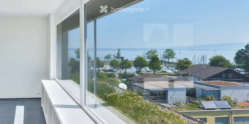 Modern balcony with large glass windows offering a scenic view of a harbor, boats, and distant water.