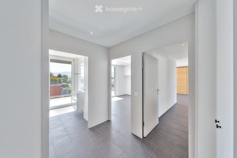 Modern, minimalist hallway with white walls, grey tiled floor, and several open doors leading to different rooms and a balcony area.