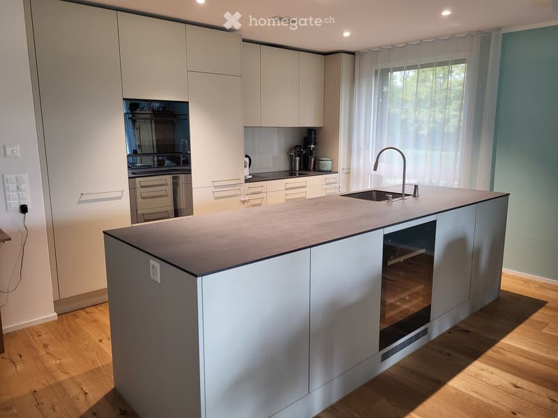 modern kitchen with white cabinetry, island with granite countertop, large windows with white curtains, built-in oven and dishwasher, and a faucet above the sink