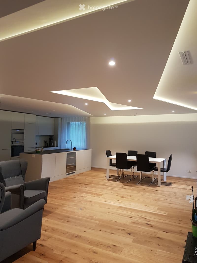 Dining area, open kitchen, wooden floor, modern ceiling design, white dining table and chairs, modern gray armchair, island with central kitchen island, faucet, gas stove, double oven, built-in appliances.