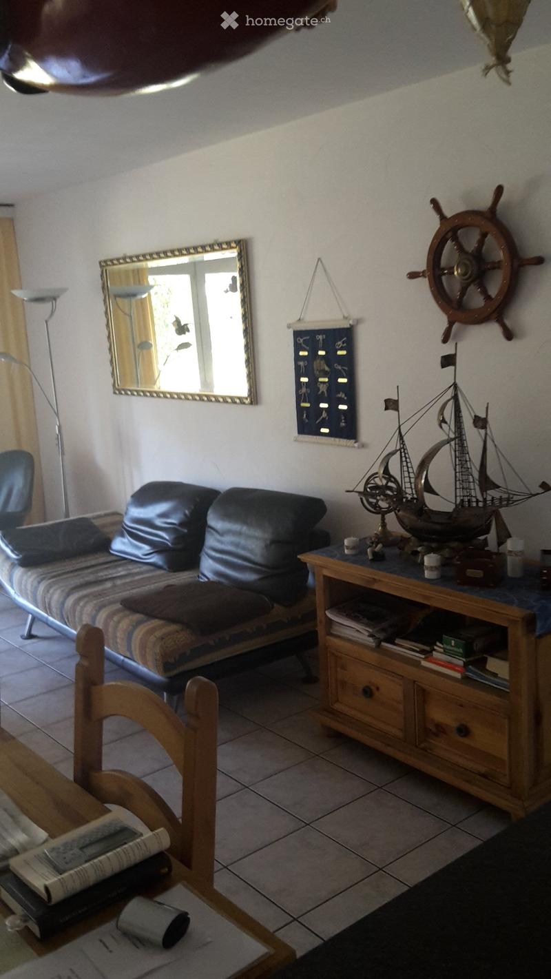 A cozy living room with a sofa, a wooden table, a chair, a mirror, a model ship, and a floor lamp.