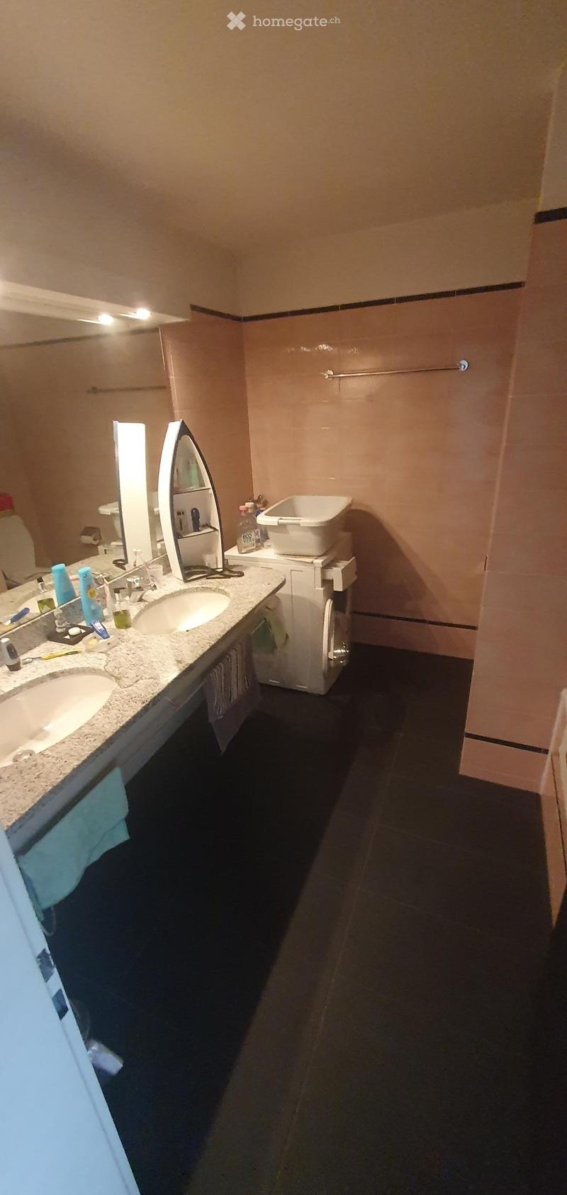 Bathroom with double sink, mirror, toilet, and various toiletries on the counter.
