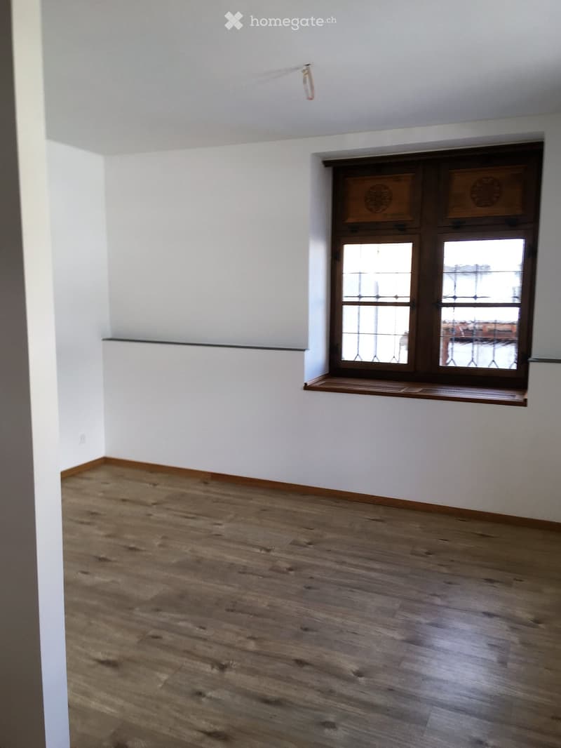 Empty room with wooden flooring and white walls, featuring a large window with decorative glass panels and a small wooden sill.