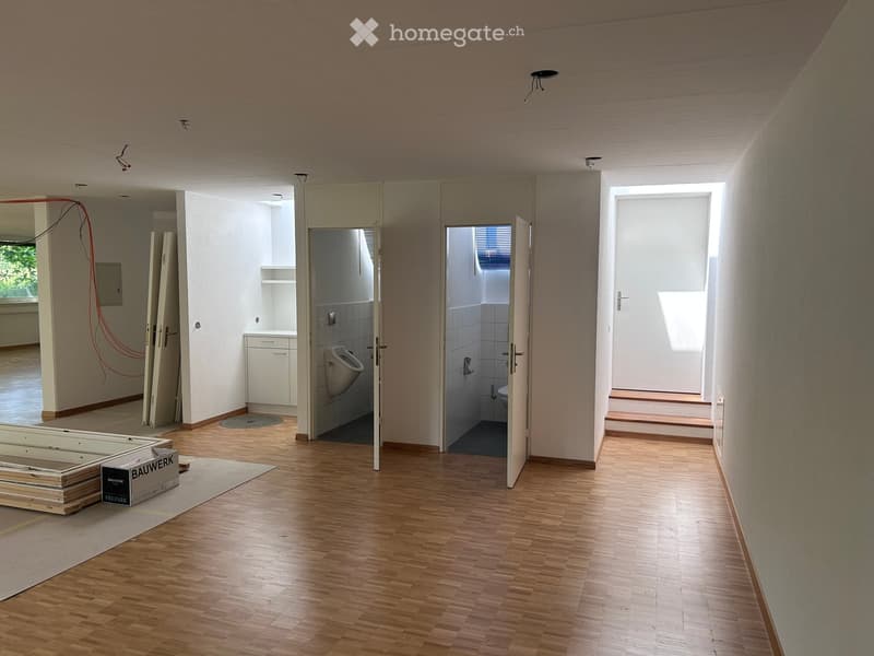 Empty hallway with wooden flooring, open doors leading to bathrooms, and exposed construction materials and boxes.
