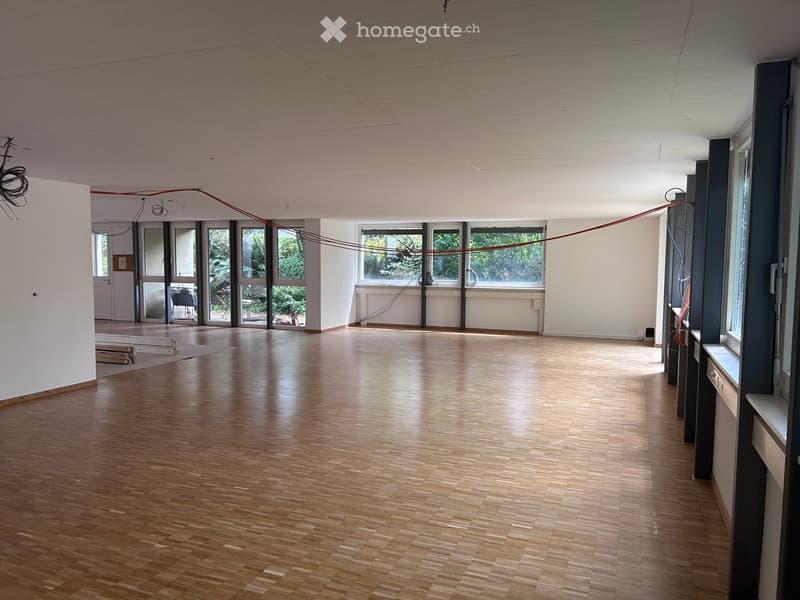 Empty room with wooden flooring, white walls, large windows, and visible electrical wires. No furniture or equipment present.