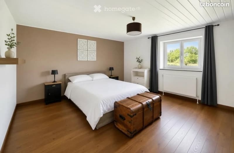 Cozy bedroom with wooden flooring, a large bed with white linens, nightstands with lamps, a chest, and decorative vases on shelves.