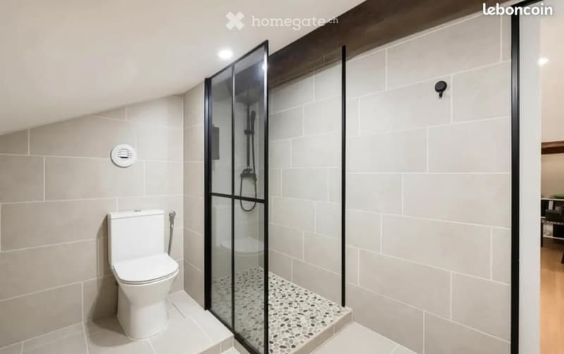 Modern bathroom with a white toilet, glass-enclosed shower, and light grey tiles.