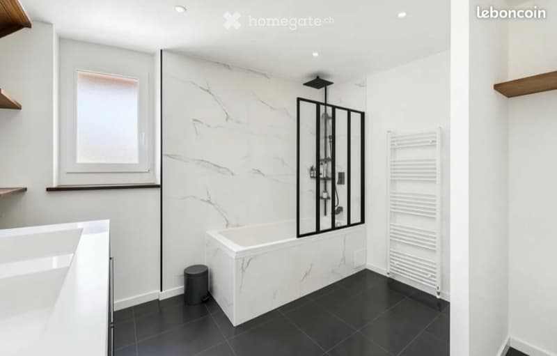 Modern bathroom with white marble walls, black tiled floor, bathtub, shower enclosure, radiator, and shelves.