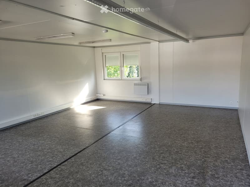 Empty room with white walls, grey tiled floor, and two windows with blinds. No furniture or equipment present.