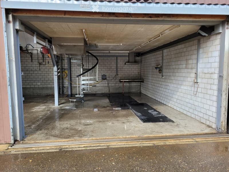 Underground garage with concrete floor, tiled walls, spiral staircase, and various pipes and equipment.