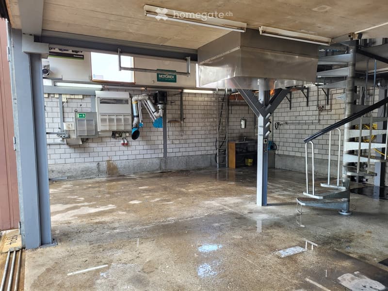 Empty industrial-style room with concrete floor, tiled walls, metal staircase, and various equipment and machinery visible.