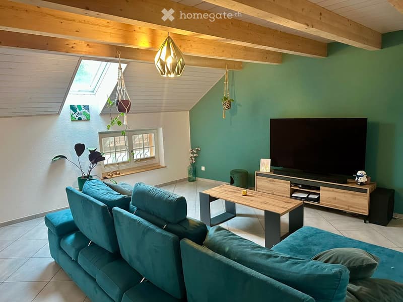 Modern living room with teal sofa, wooden coffee table, flat-screen TV on wooden stand, hanging plants, and decorative items.