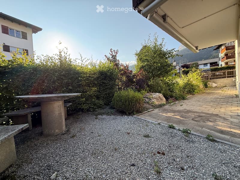 Garden area with a stone table, bench, gravel ground, and surrounding greenery.
