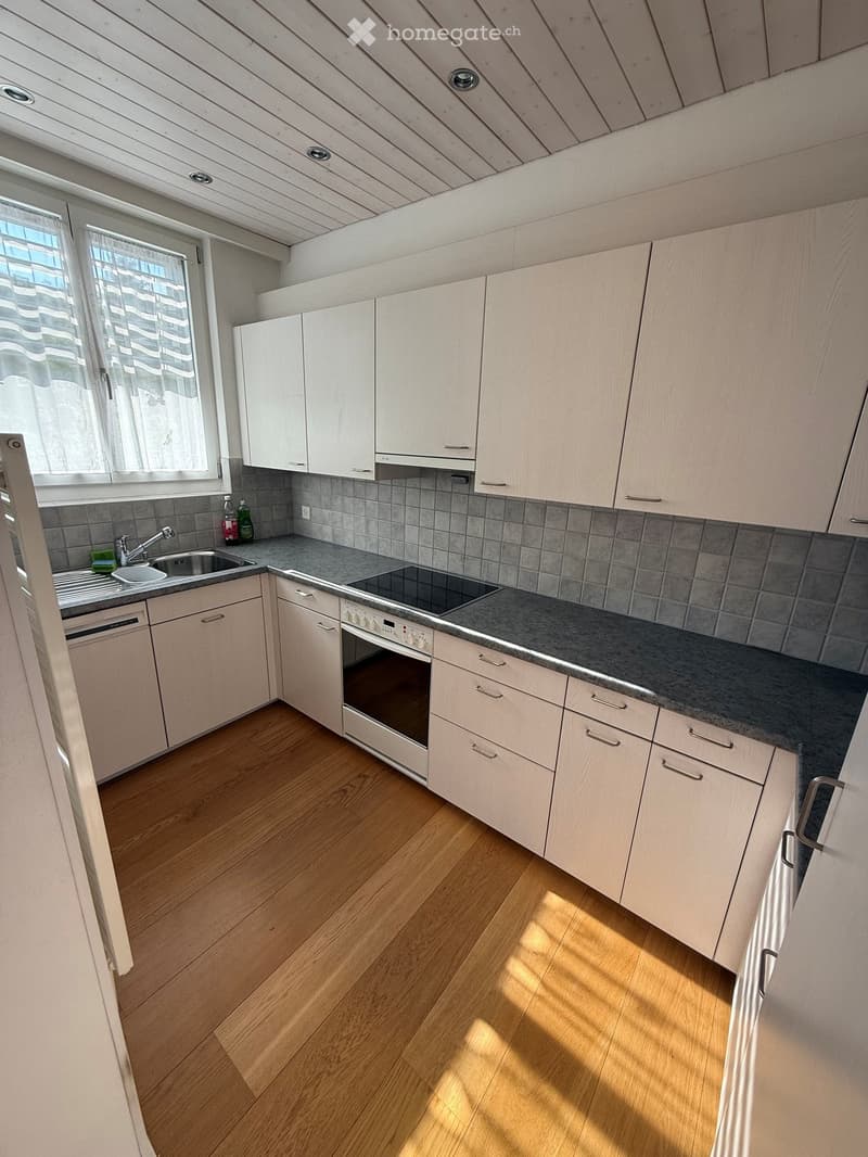 Modern kitchen with light wooden cabinets, stainless steel appliances, and a grey tiled backsplash.
