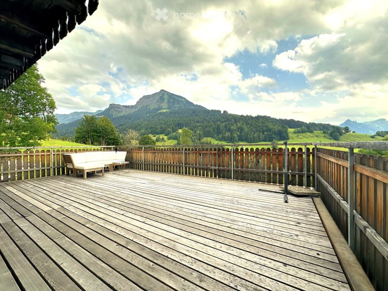 Wooden deck with a white sofa and small table, overlooking a scenic mountain landscape.