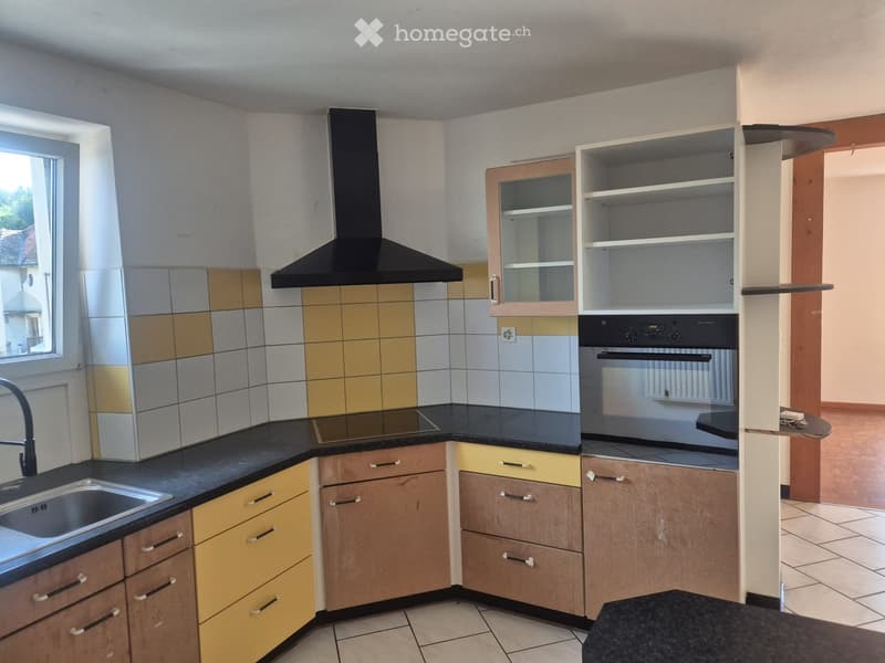 Modern kitchen with black countertops, wooden and yellow cabinets, stainless steel sink, and built-in oven with range hood.