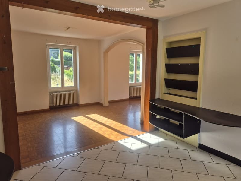 Empty room with wooden flooring, large windows, built-in shelving, and a radiator. No furniture or equipment present.