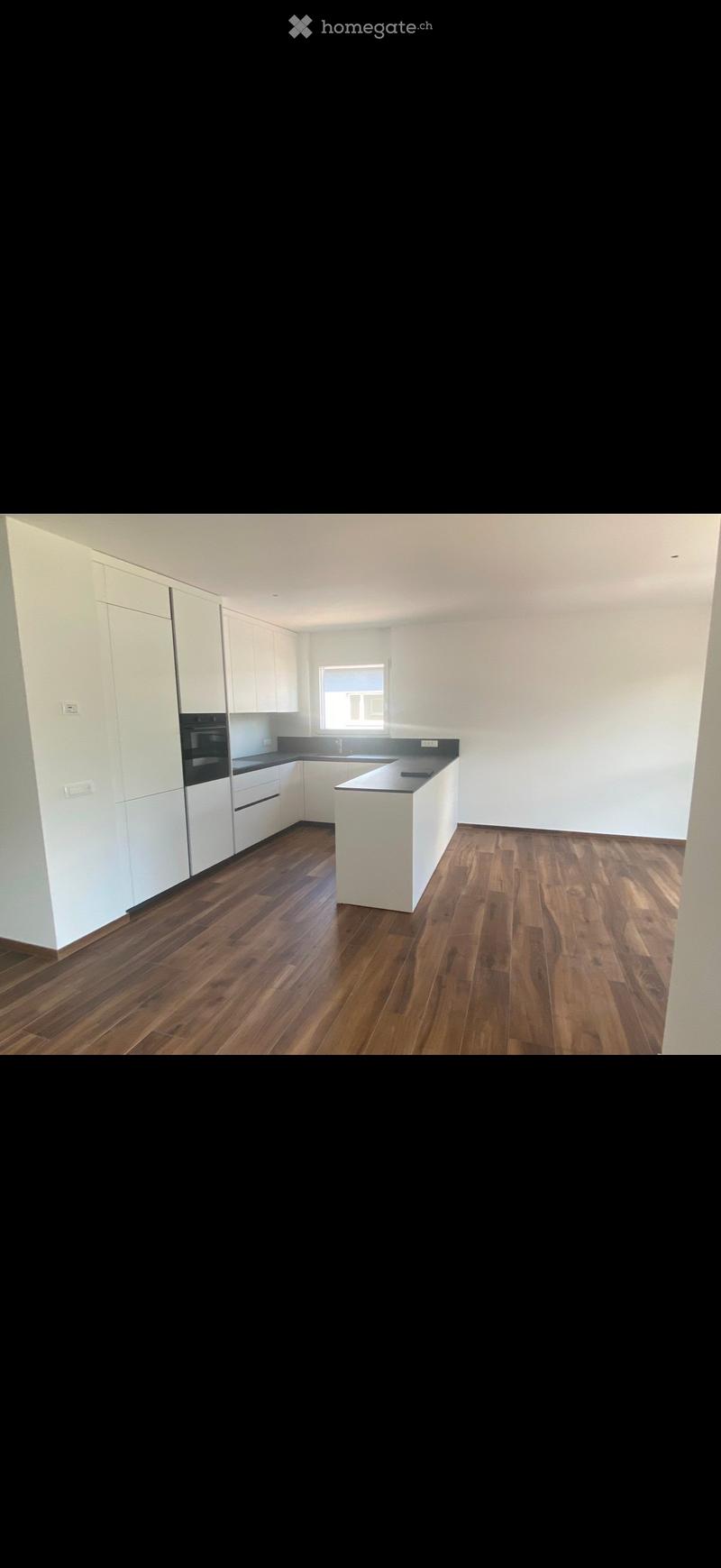 Empty kitchen with white cabinets, dark countertops, and wooden flooring. No appliances or furniture are present.