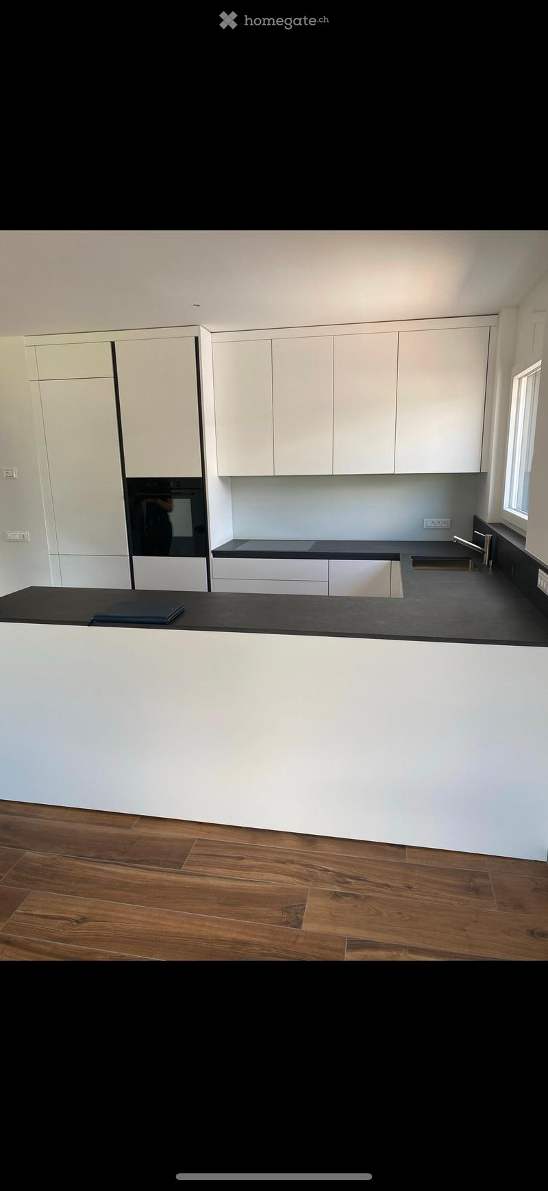 Modern kitchen with white cabinets, black countertops, and a wooden floor. Features a sink, faucet, and an oven.