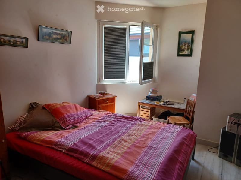 Bedroom with a single bed, nightstand, desk, chair, and framed pictures on the walls. The window is open, allowing natural light to enter.