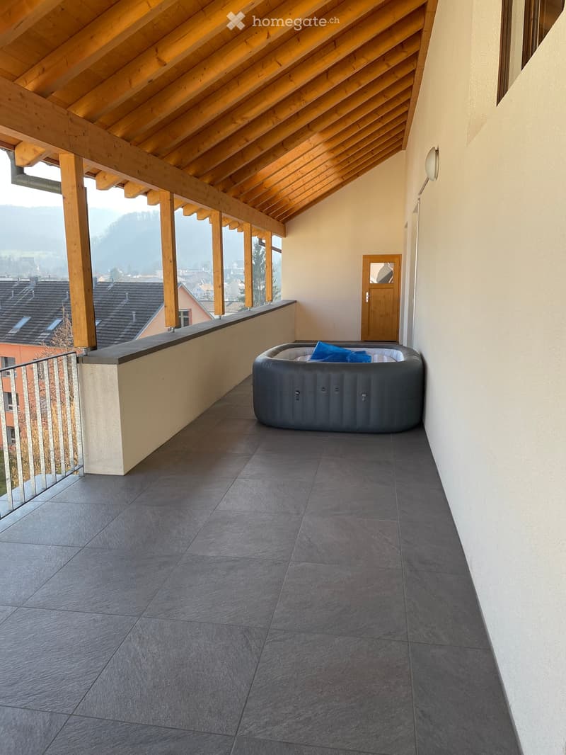 Balcony with a modern hot tub, wooden beams, and a scenic view of the town and mountains.