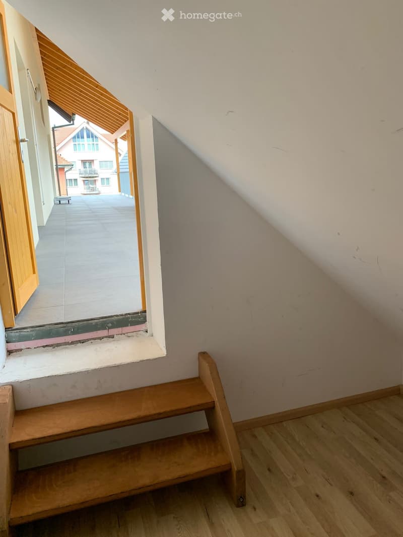 Empty wooden staircase leading to an open doorway with a view of an outdoor area and neighboring building.