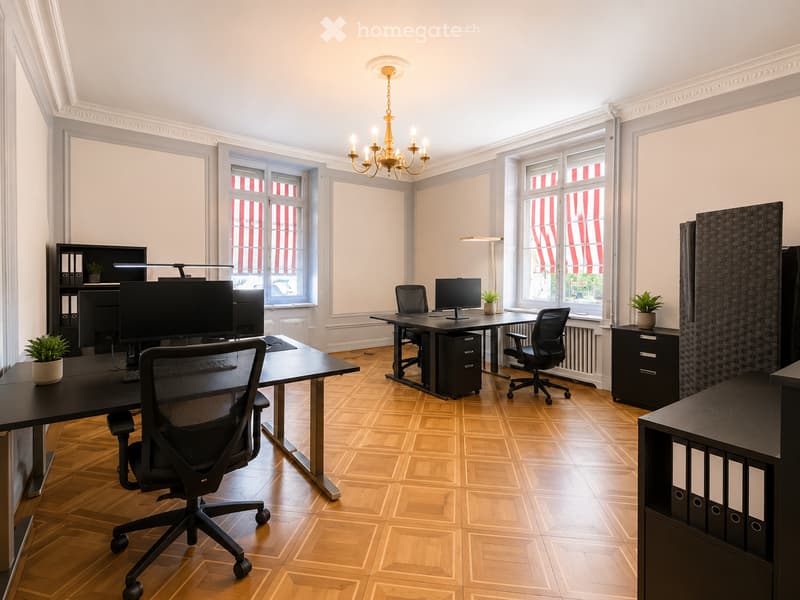 Modern office space with wooden flooring, large windows, multiple desks, office chairs, computer screens, cabinets, and decorative plants.