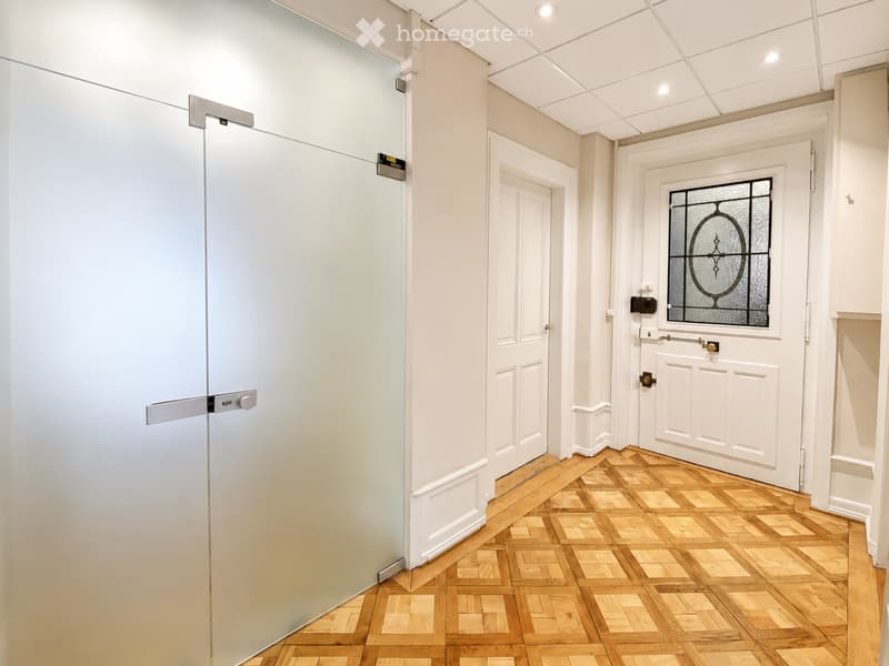 A narrow hallway with wooden flooring, white walls, and several doors including a frosted glass door with decorative glass panels.