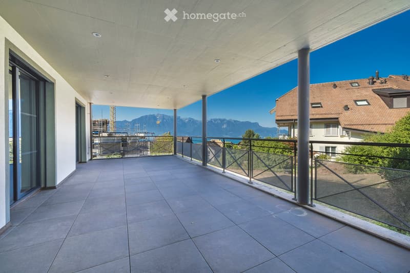 Modern balcony with tiled floor, glass railing, and a view of mountains and a lake.