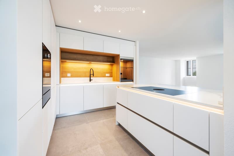 Modern kitchen with white cabinets, a central island, and built-in lighting. Features a sleek design with a wooden accent shelf and a stainless steel sink.