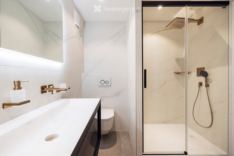 Modern bathroom with white marble walls, a sleek sink, a toilet, and a glass-enclosed shower with a rainfall showerhead.