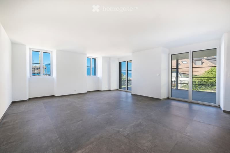 Empty room with white walls, dark tiled floor, large windows, and sliding glass doors leading to a balcony.