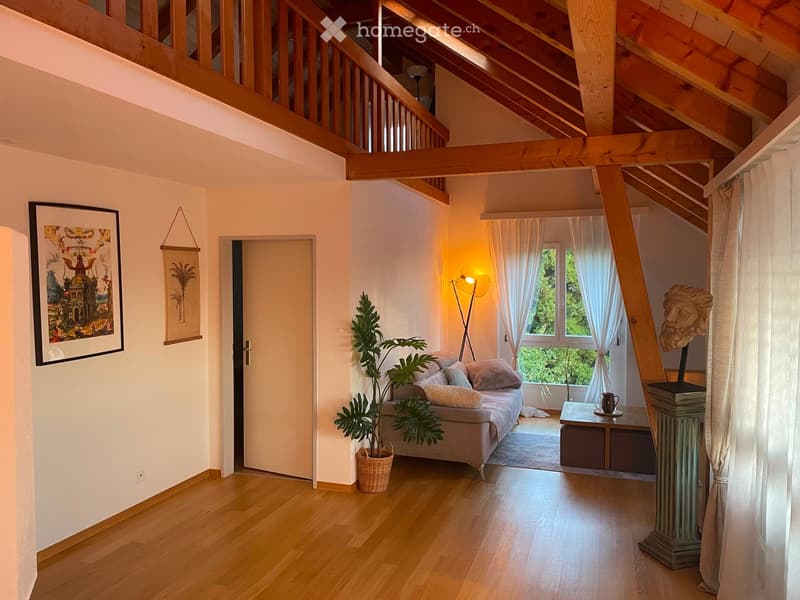 Bright living room with wooden floors, exposed wooden beams, large windows with white curtains, a sofa, a small table, a plant, and artwork on the walls.