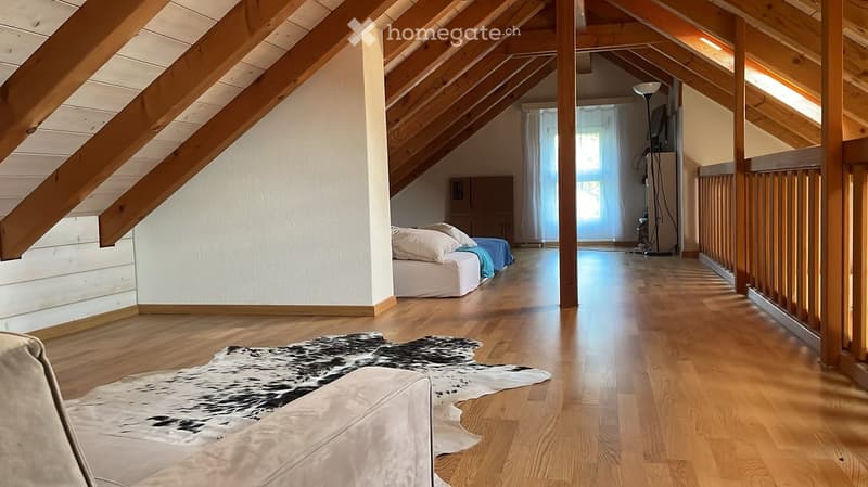 Spacious attic room with wooden beams, hardwood floors, a bed, a sofa, a large cowhide rug, and large windows with curtains.