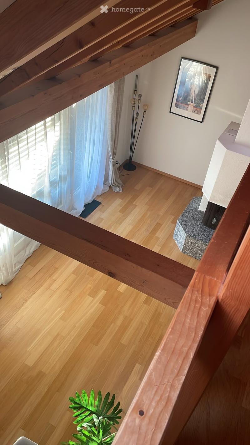 A modern hallway with wooden flooring, white walls, and a staircase leading to an upper level. Features include a large window with white curtains, a floor lamp, a framed picture, and a small plant on the lower level.