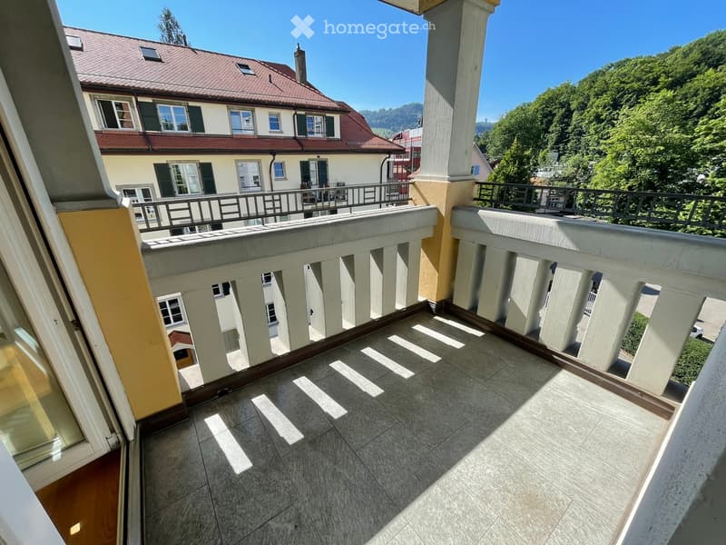 Balcony with tiled floor, white balustrade, overlooking a residential building and green landscape.