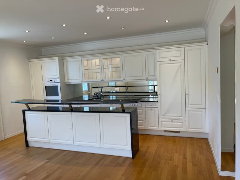 Modern kitchen with white cabinets, black countertop, and wooden flooring.
