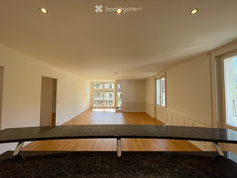 Empty room with wooden flooring, white walls, and large windows allowing natural light. No furniture or furnishings are present.