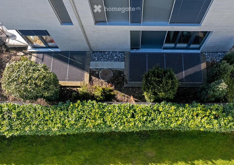 Aerial view of a modern house with a well-maintained garden, featuring a neatly trimmed hedge, small shrubs, and a gravel pathway leading to the building.