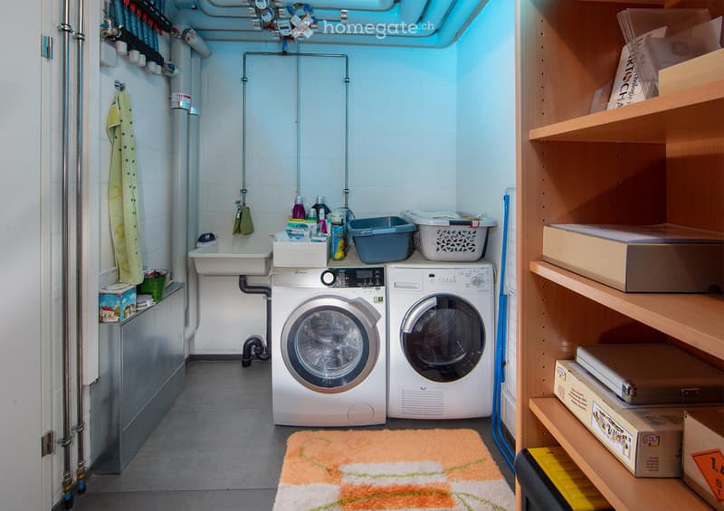 Functional bathroom with a washing machine, dryer, sink, and shelves for storage. Includes a towel hanging on the wall and a small rug on the floor.
