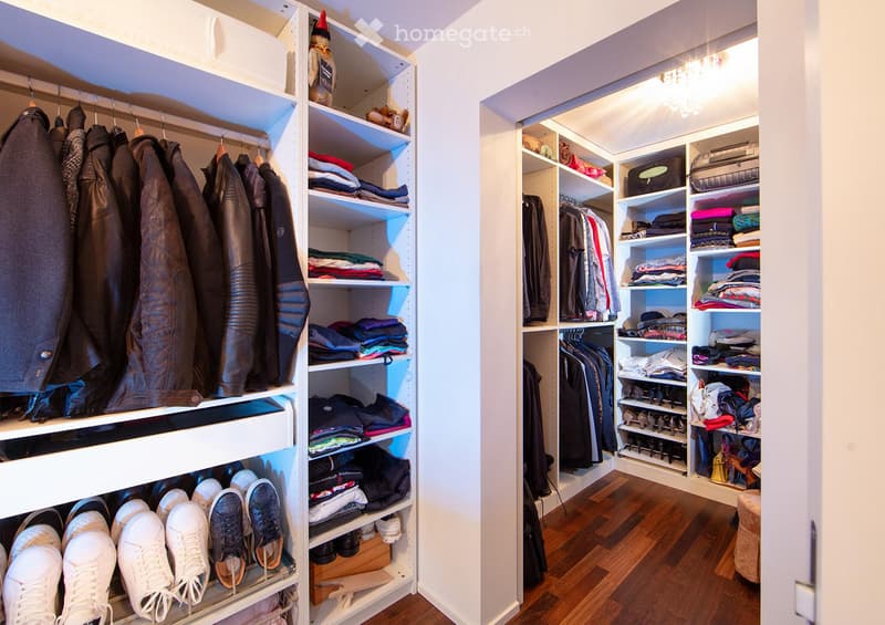A well-organized walk-in closet with multiple wardrobe sections, shelves filled with folded clothes, and rows of shoes neatly arranged on the floor.