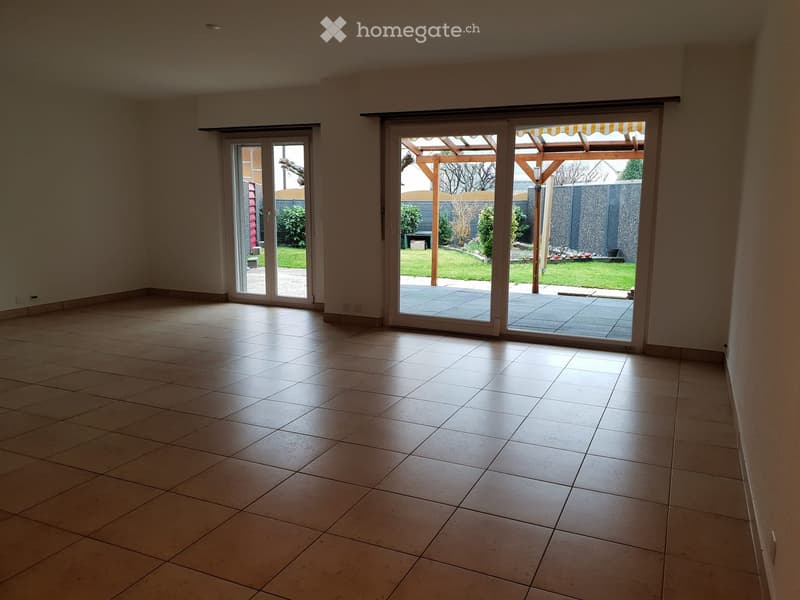 Empty room with tiled floor and large sliding glass doors leading to a patio and garden area.
