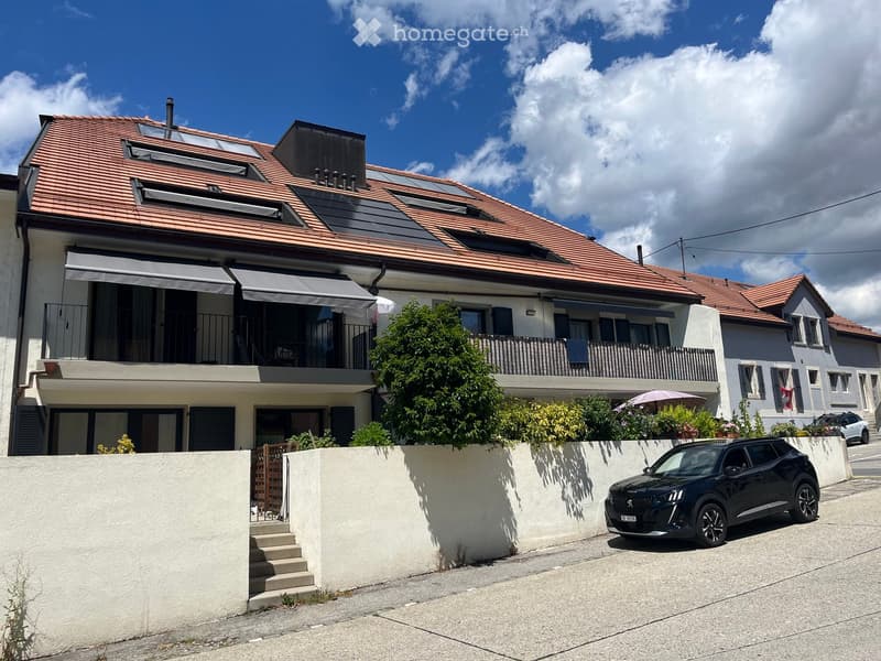 Two-story house with red-tiled roof, multiple balconies, and solar panels on the roof. A black SUV is parked in front of the house.
