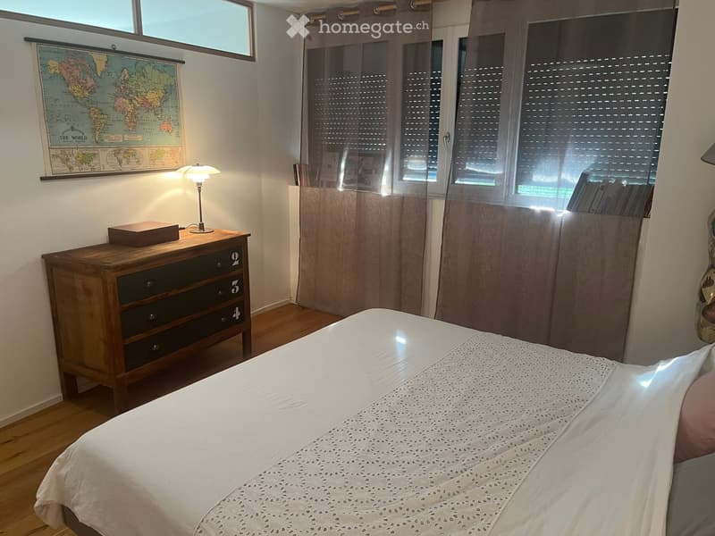 Cozy bedroom with a wooden bed, white bedding, a nightstand with a lamp, a wooden drawer unit, and a world map on the wall.
