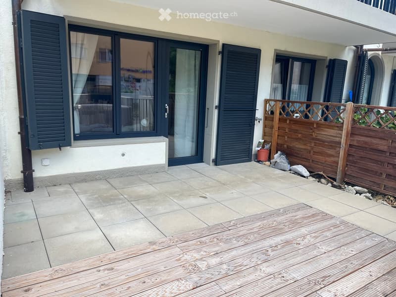 Balcony area with tiled floor, wooden deck, wooden fence, and large windows with shutters leading to the interior.