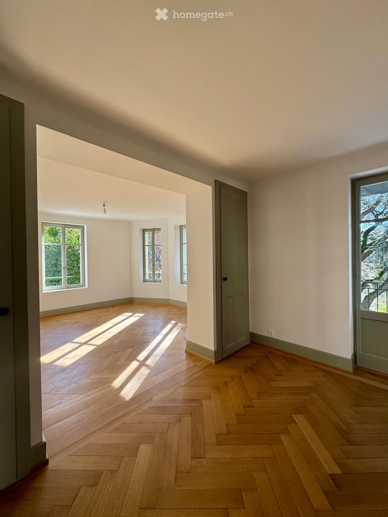 Empty room with parquet flooring, white walls, three windows with natural light, doors