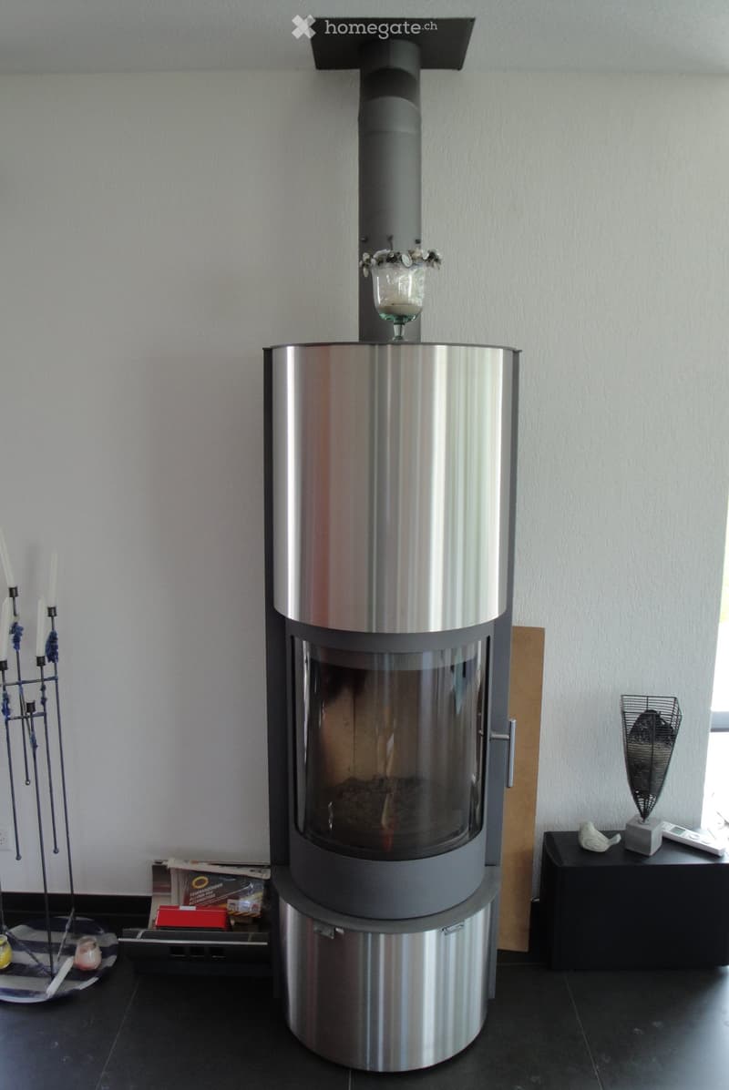 Modern living room with a sleek, stainless steel fireplace as the focal point, accompanied by a candle holder, small table, decorative fan, and remote control on a side table.